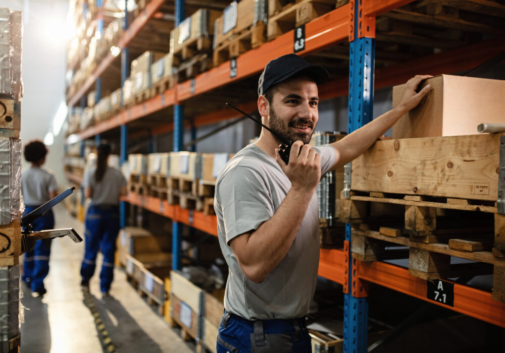 Happy dispatcher using walkie-talkie while working in distribution warehouse.