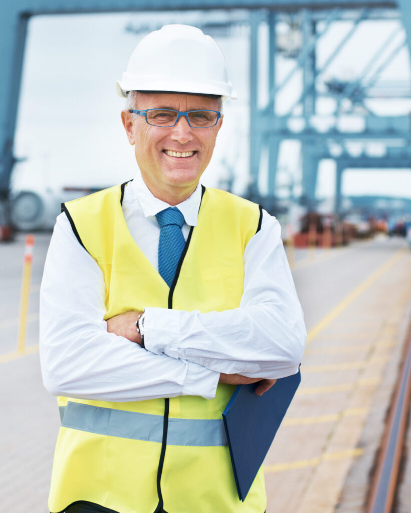 Portrait of a dock worker standing at the harbor amidst shipping industry activity.