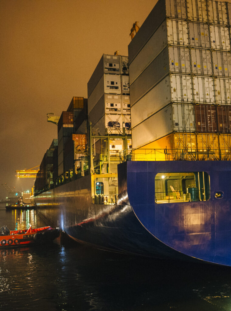 Tugboat manoeuvring container ship on river at night, Tacoma, Washington, USA